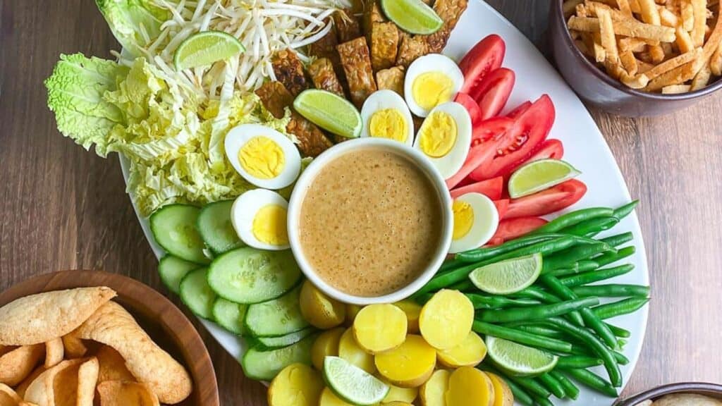 overhead-horizontal-image-of-white-oval-platter-holding-Low-FODMAP-Gado-Gado-with-dishes-of-shrimp-crackers-alongside-on-wooden-surface.