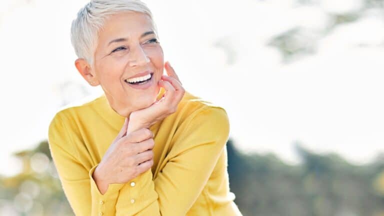 Confident older woman in yellow with short grey hair.