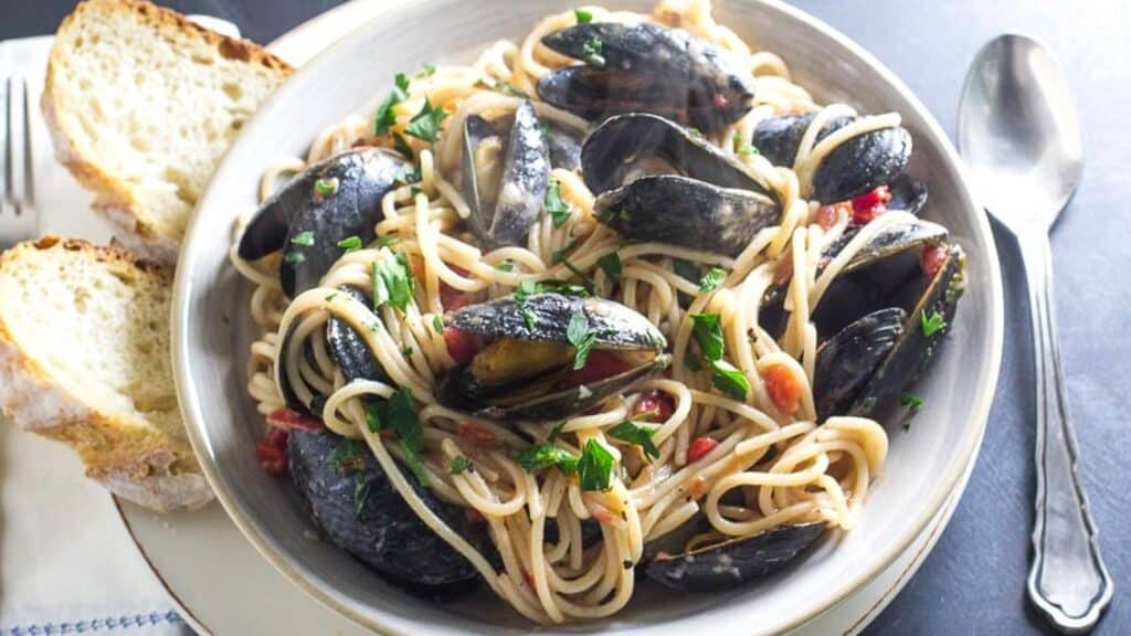 Pasta-with-Mussels-in-a-white-bowl-with-bread-alongside.