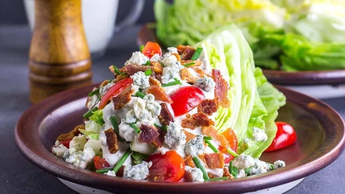 Wedge-Salad-slathered-with-blue-cheese-dressing-on-a-brown-ceramic-plate.