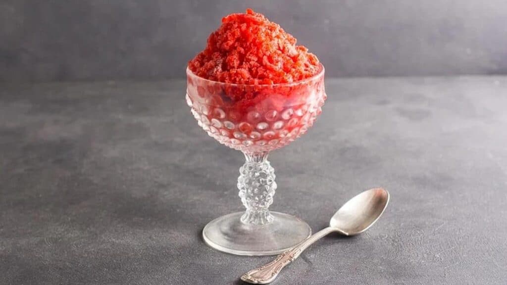 Strawberry-Granita-in-a-clear-glass-footed-dish-with-a-silver-spoon-on-a-dark-gray-background.