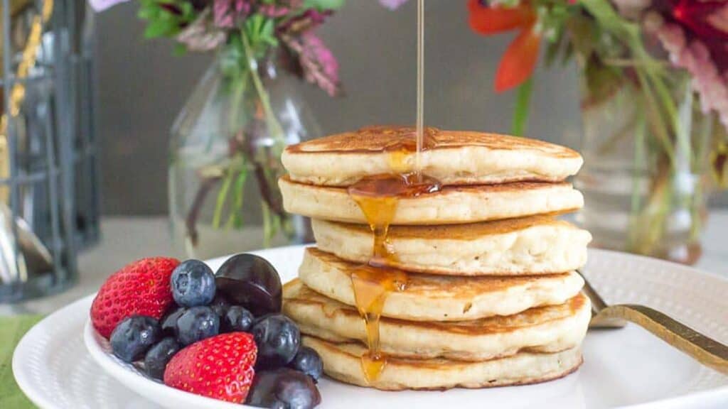 a-perfect-stack-of-low-FODMAP-FLUFFY-Pancakes-on-a-white-plate-syrup-pouring-over-top-fruit-salad-on-the-side.