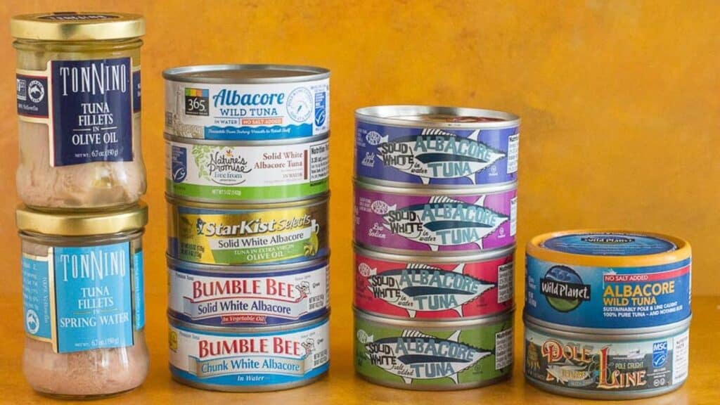 assorted-cans-and-glass-jars-of-tuna-against-a-dark-yellow-background.