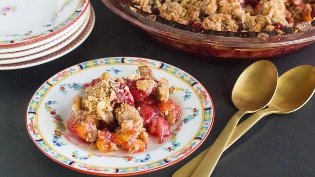 horizontal-image-of-low-FODMAP-strawberry-peach-crisp-on-a-decorative-plate-and-in-pie-plate-in-background.