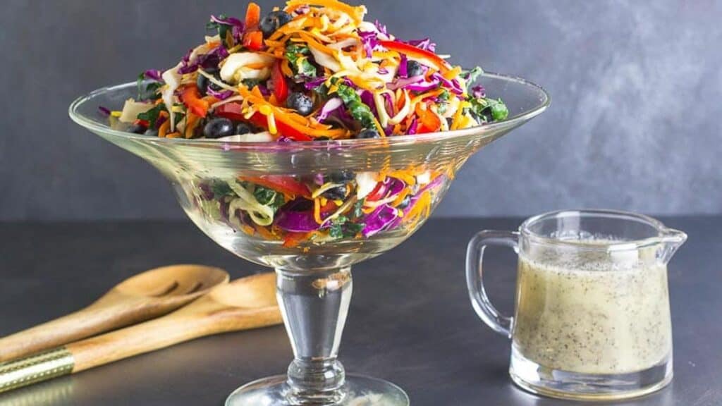 Eat-the-Rainbow-Slaw-in-a-footed-glass-bowl-with-poppy-seed-dressing-alongside.