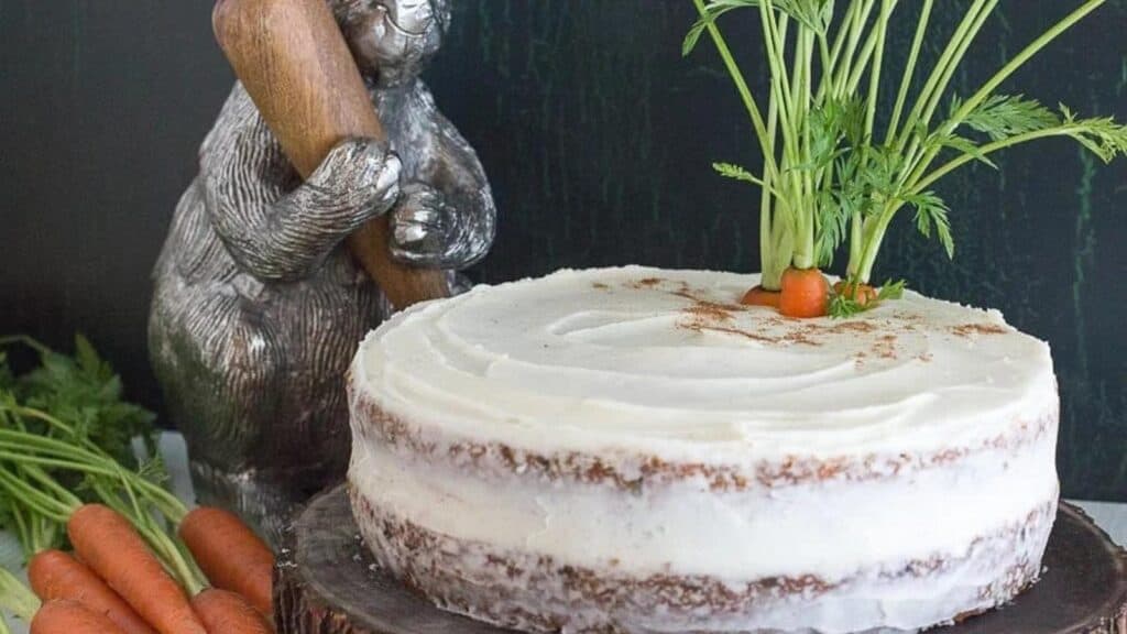 carrot-cake-with-cream-cheese-frosting-on-a-wooden-plate-with-decorative-bunny-in-the-background.