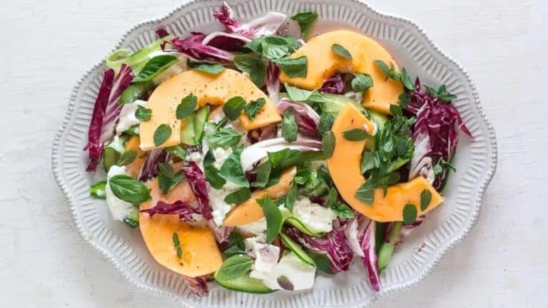 cantaloupe-cucumber-and-burrata-salad-with-herbs-on-a-white-platter-and-white-wooden-surface.