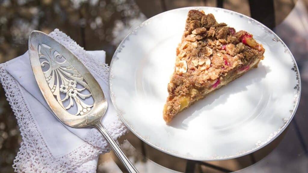 overhead-shot-of-slice-of-Low-FODMAP-Rhubarb-Cheesecake-Tart-on-white-plate-oustide-on-glass-table.