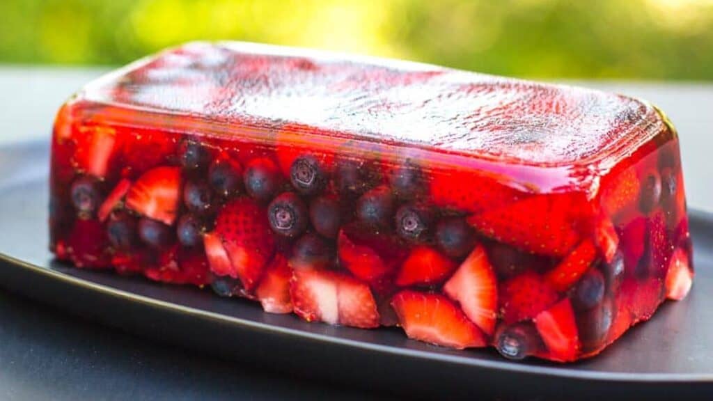 side-view-of-Low-FODMAP-Mixed-Berry-Terrine-on-an-oval-black-plate-outside-on-deck-garden-in-background.