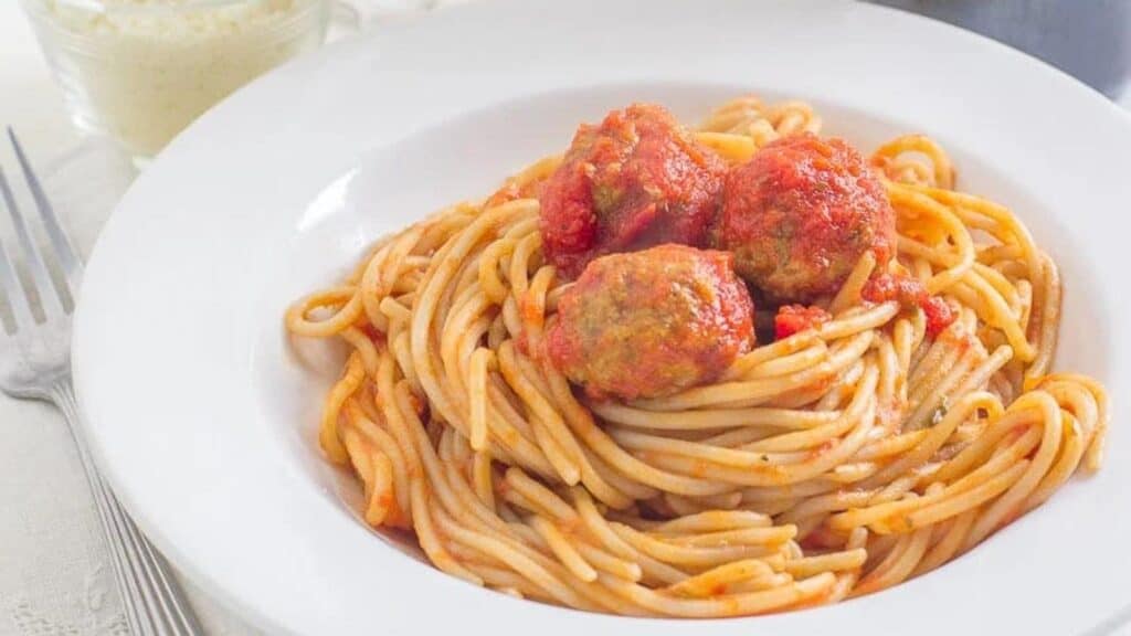 spaghetti-meatballs-in-a-white-bowl-with-Parmesan-cheese-in-a-small-bowl-in-the-background.