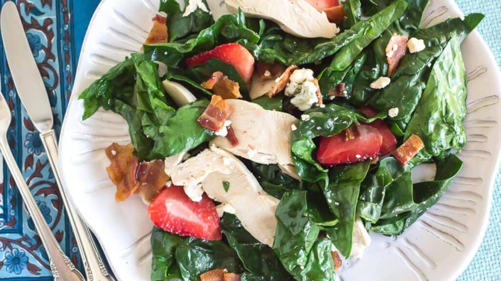 spinach-salad-with-bacon-blue-cheese-and-strawberries-on-a-white-plate-overhead-shot.