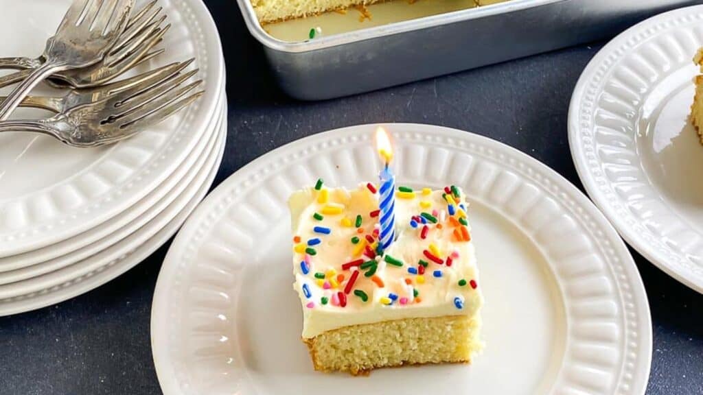yellow-snack-cake-with-buttercream-rainbow-sprinkles-and-blue-candle-on-white-plate-1.
