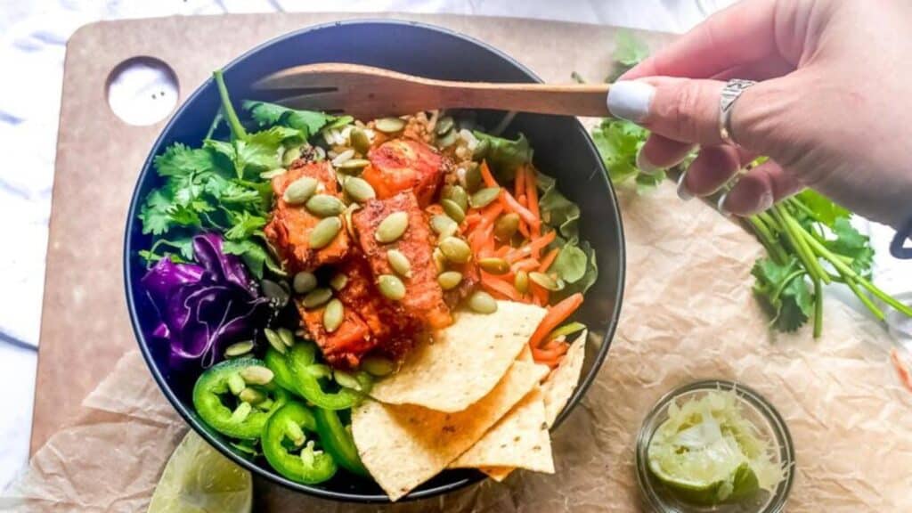 Baja-Tempeh-Taco-Salad-in-dark-bowl-womans-hand-holding-wooden-fork-e1662211606807.