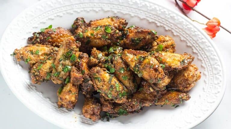 Pok-Pok-Chicken-Wings-on-oval-white-plate-with-coral-colored-flowers-in-background.