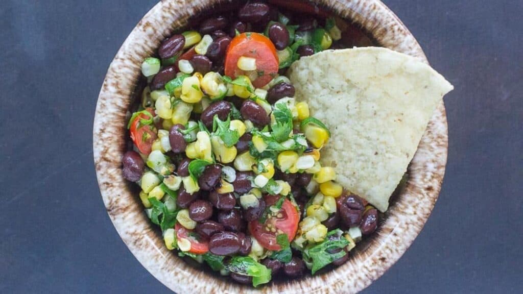 grilled-corn-salsa-with-black-beans-in-a-small-bowl-and-a-corn-chip-for-dipping.