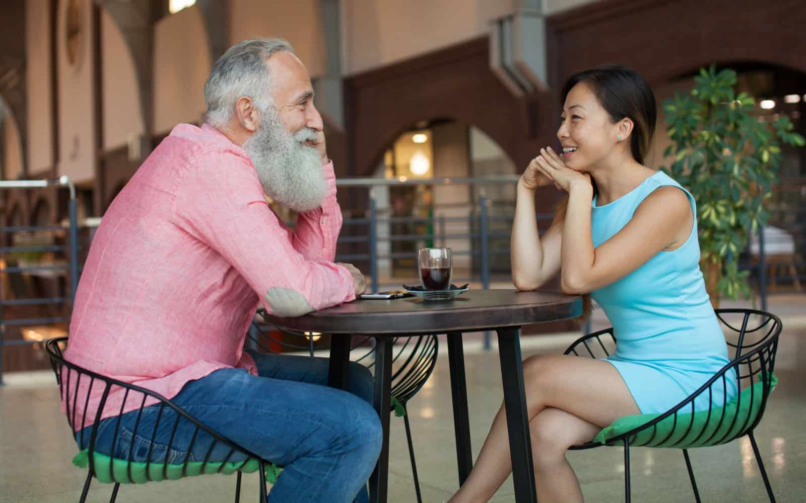 Couple eating food at Cafe. Happy multiracial couple outside. Bearded senior man, Asian woman.
