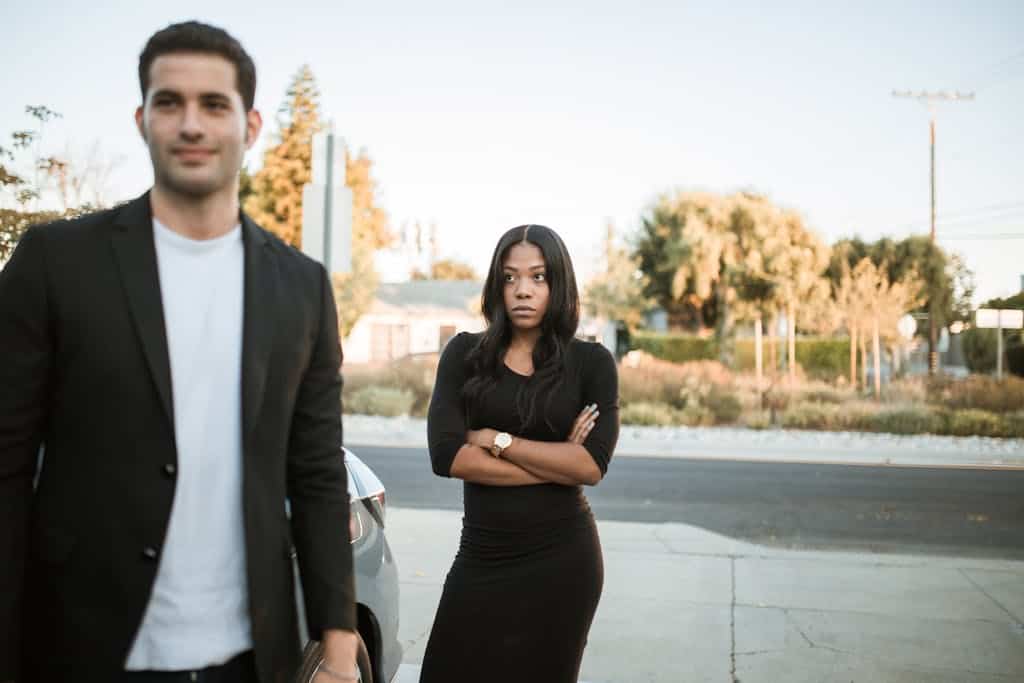 A couple facing relationship tension outdoors with arms folded, expressing emotions.
