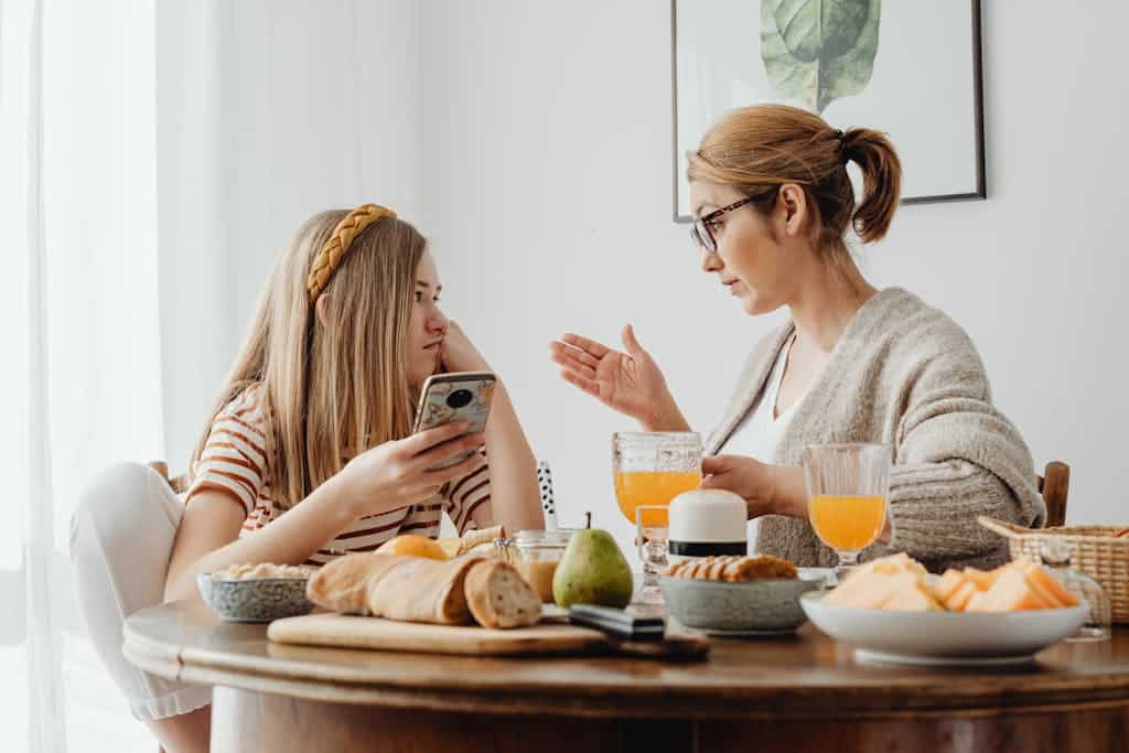 A mother and daughter engage in a conversation over breakfast, with an array of food on the table.