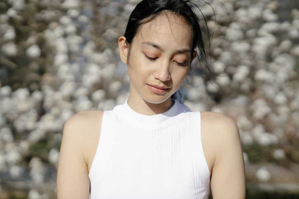 A serene young woman enjoys a sunny day in a garden, deep in thought.