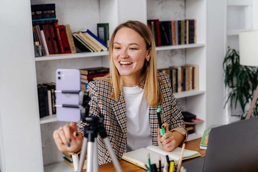A woman conducts an online lesson from her home office, using a smartphone and a laptop.
