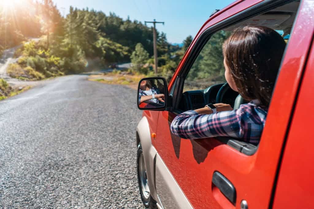 A woman enjoys a road trip through a sunny forest in her red SUV, capturing a moment of freedom and adventure.