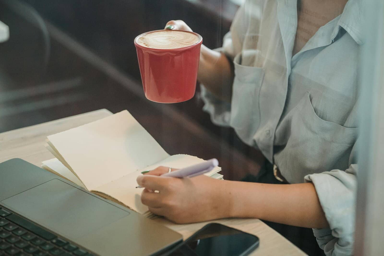 A woman writes in a notebook while enjoying a coffee in a cozy café setting.