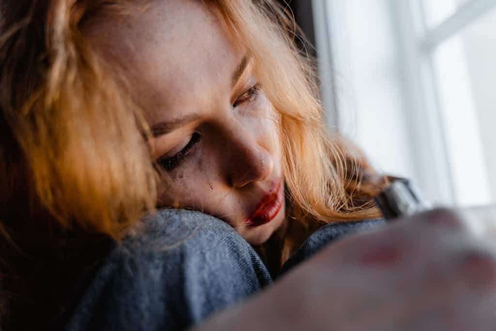Close-up of a woman with red hair in a thoughtful and emotional moment indoors.