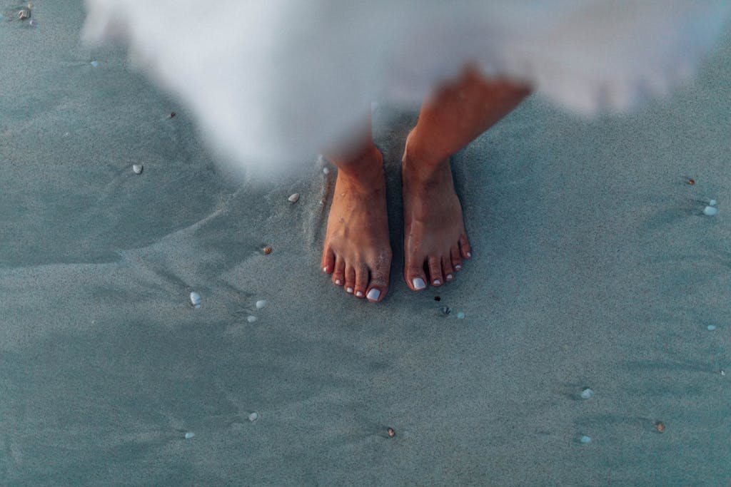 Close-up of woman's feet on sand near the ocean, creating a serene summer vibe.