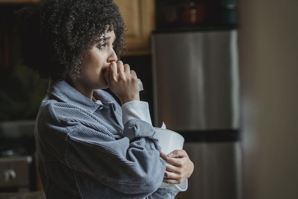 Side view of crying African American female with tissue sorrowing from unhappiness and grief in kitchen