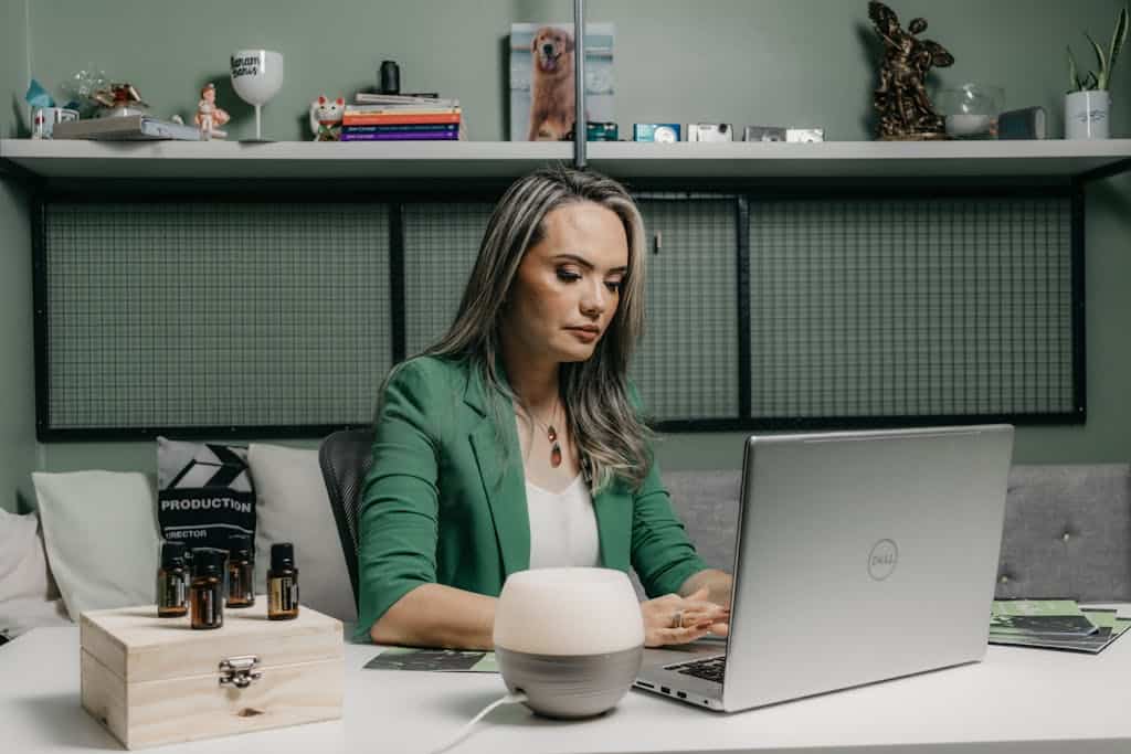Woman in green jacket working on a laptop in a home office environment with essential oils.