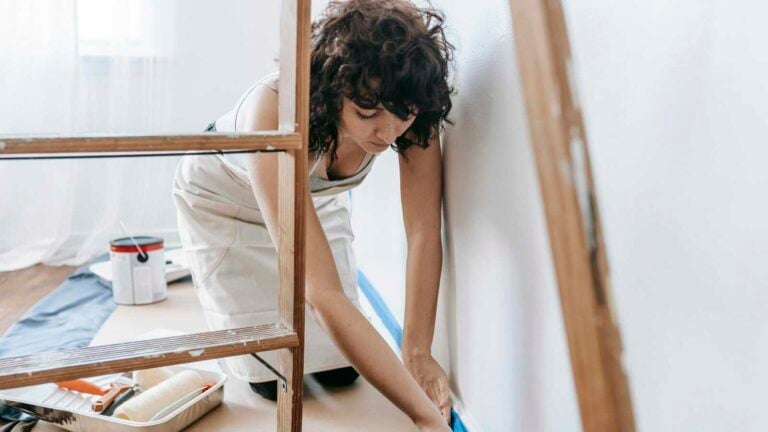 Woman uses tape to prep wall for painting, part of a DIY home renovation project indoors.