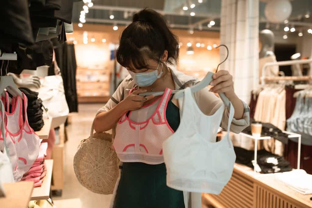 Woman wearing a mask choosing sports bras in a store during pandemic times.