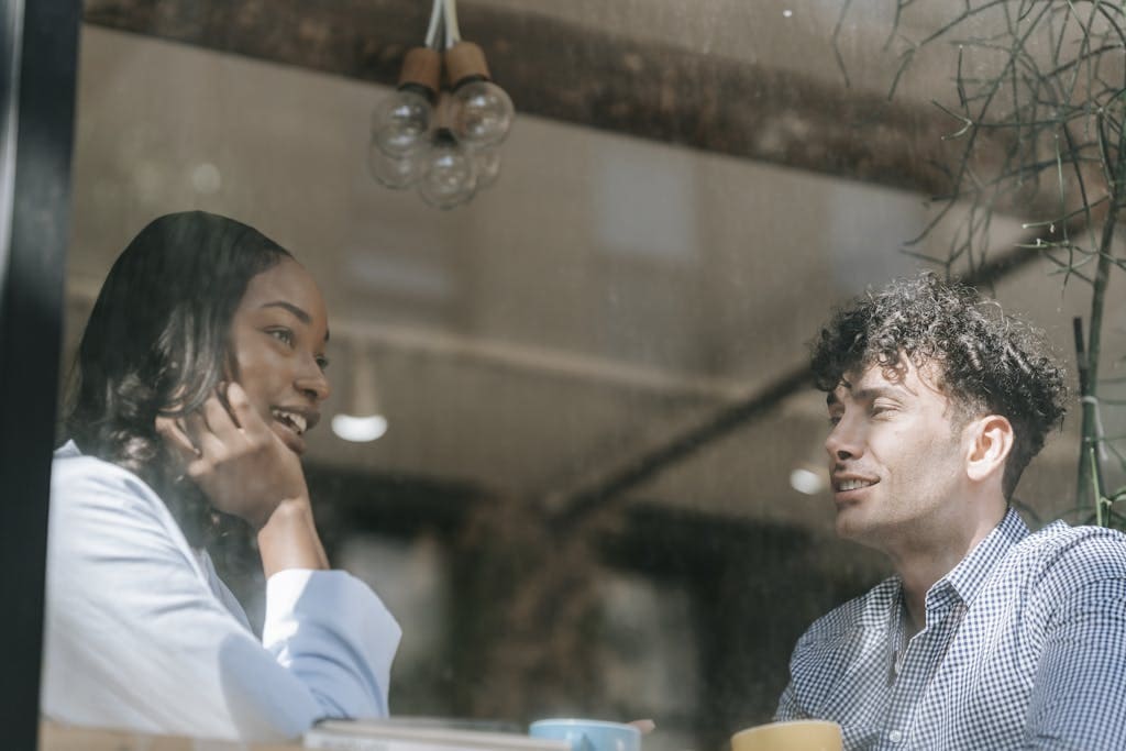 Two people enjoying a warm conversation through a cafe window, highlighting relaxed and friendly interactions.
