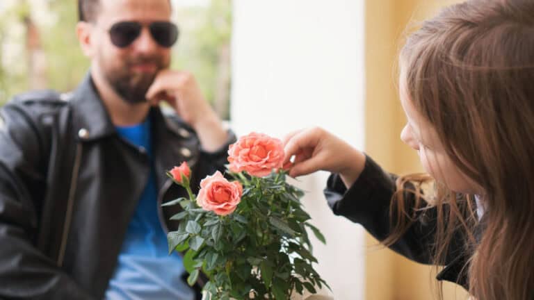 Girl touches the roses that stand on the table of the restaurantaEUR(TM)s summer terrace. In the background, in the unfocusing of her, Dad looks and smiles