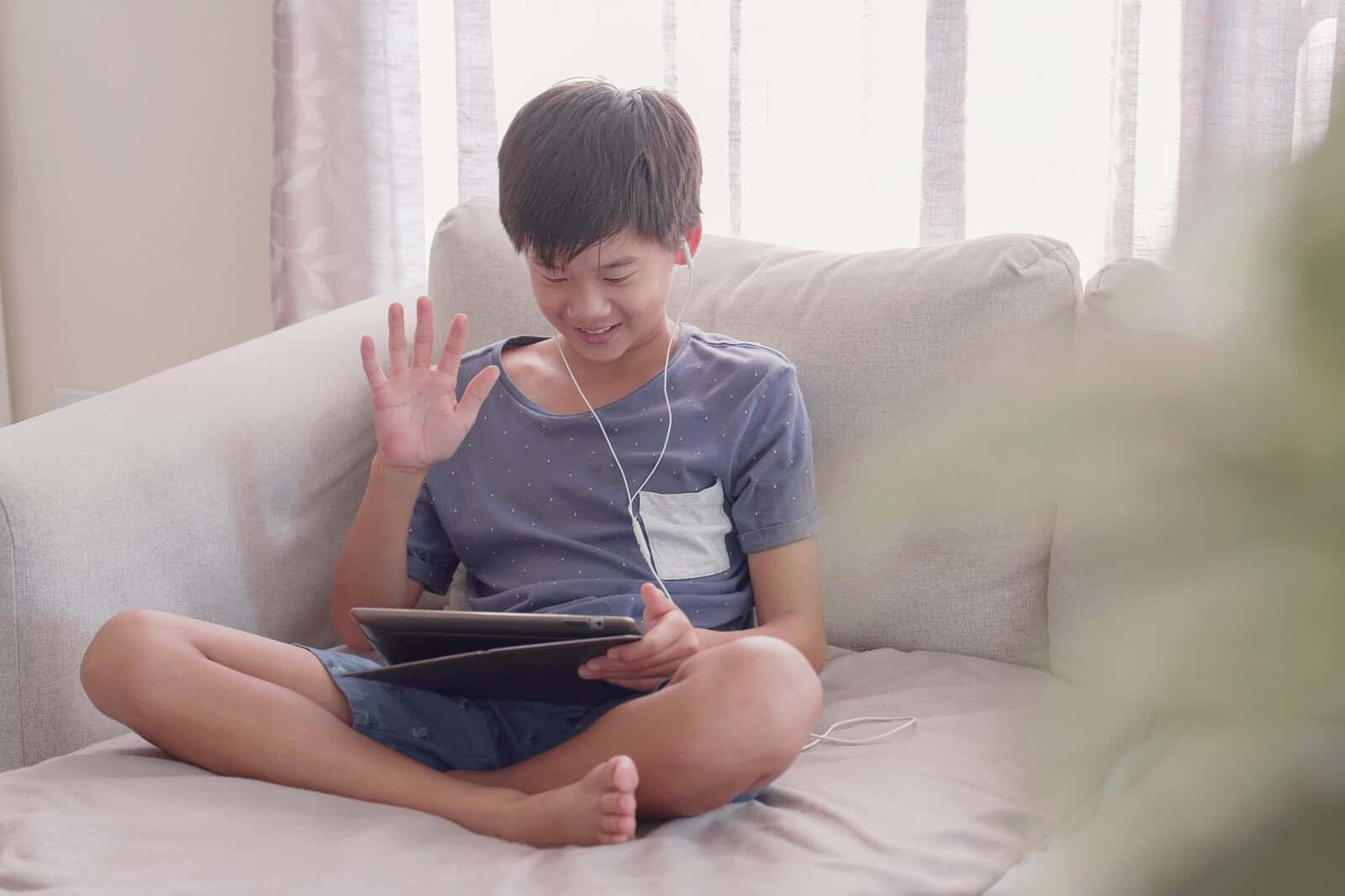 Young mixed Asian preteen boy using digital tablet at home, podcast, gaming, online education, learning remotely, homeschooling, social distancing, isolation, using facetime or zoom app concept