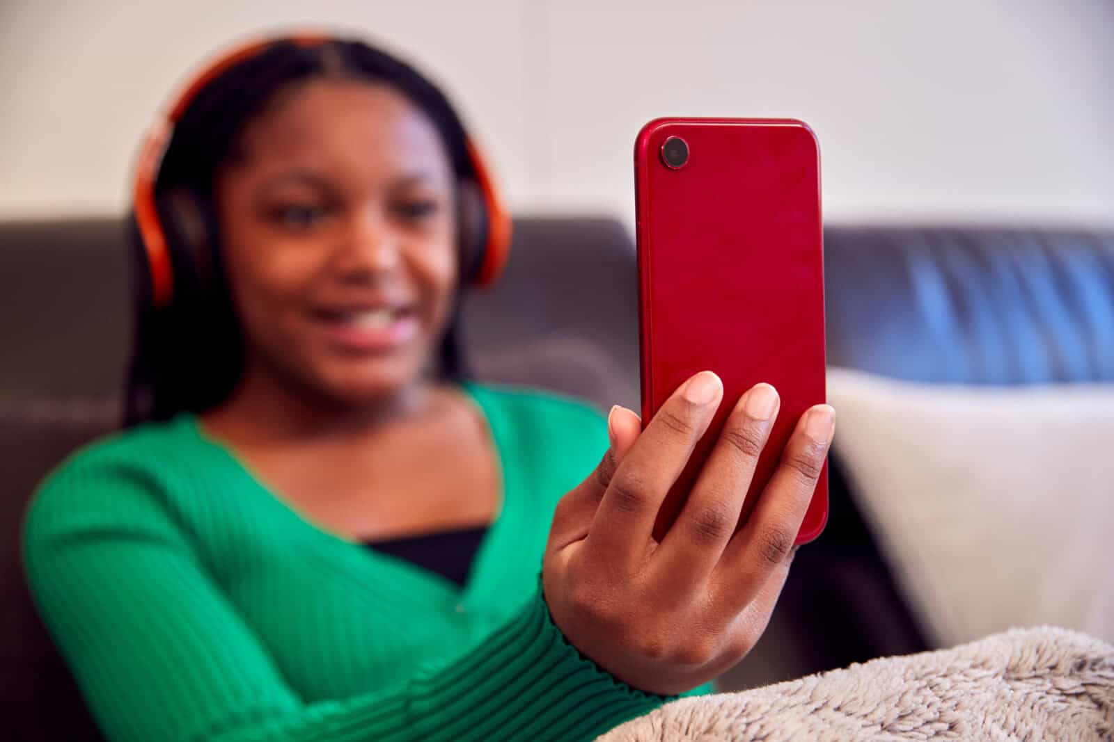 Teenage Girl Wearing Wireless Headphones Listening To Music Steaming From Mobile Phone At Home