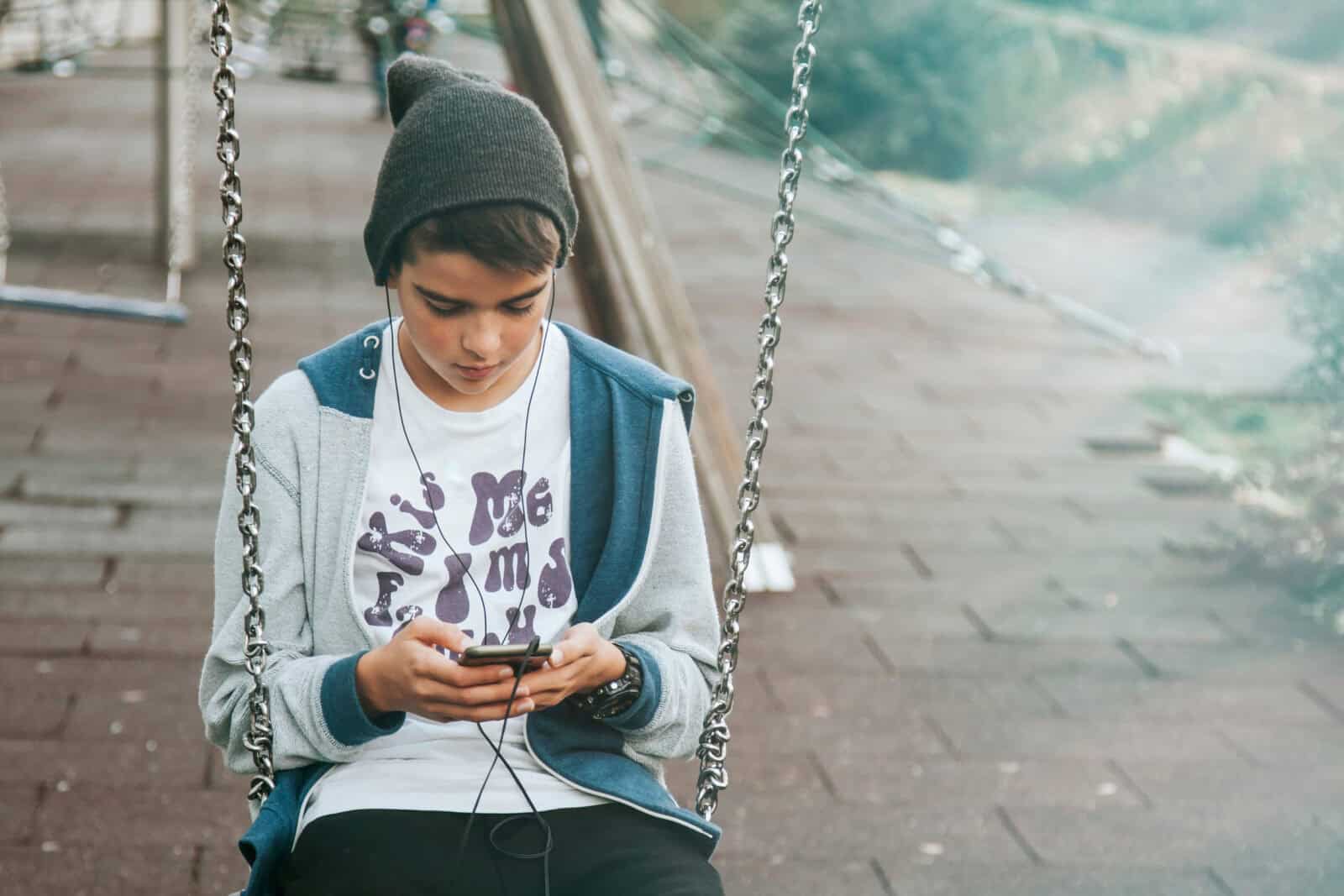 child with mobile phone on swing on city street