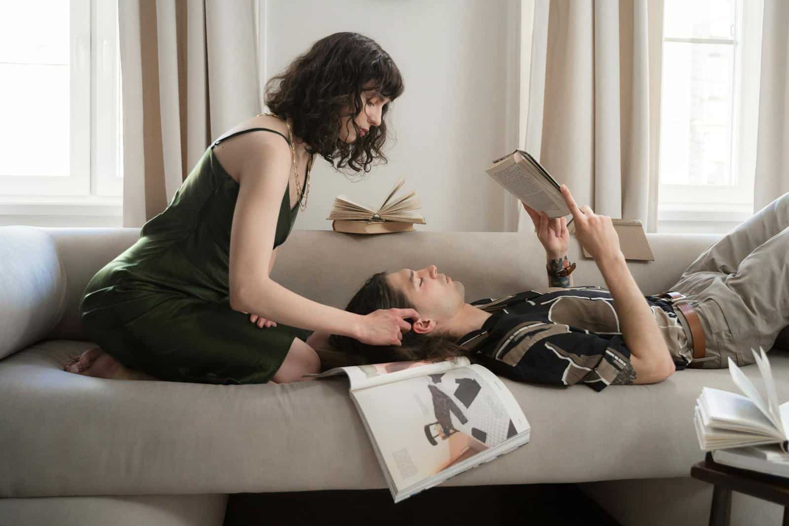 A couple relaxing indoors as one reads and the other touches hair, creating a serene and intimate atmosphere.