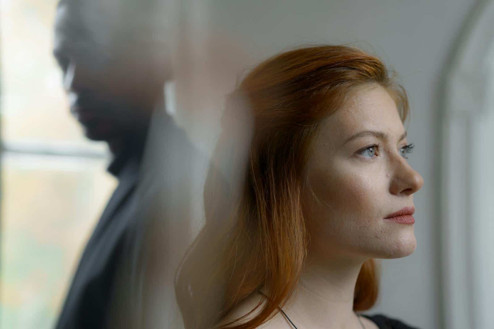 Reflective portrait of two individuals with focus on a side view woman indoors.