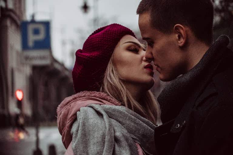 A couple shares a romantic moment in a city street during winter, capturing love and intimacy.