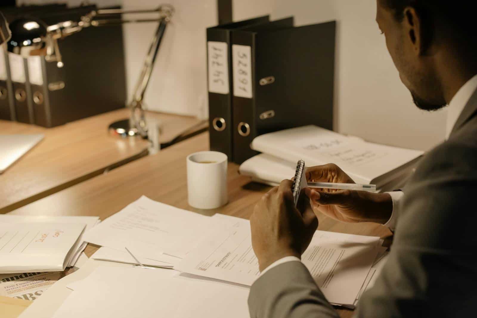 Man in gray suit reviewing documents at an organized workspace.