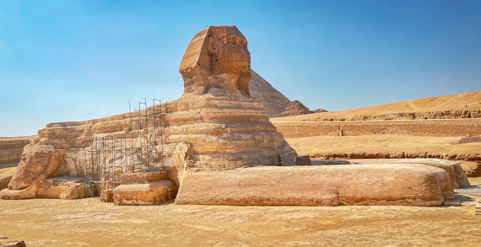 The iconic Great Sphinx of Giza with scaffolding for restoration under a clear blue sky.