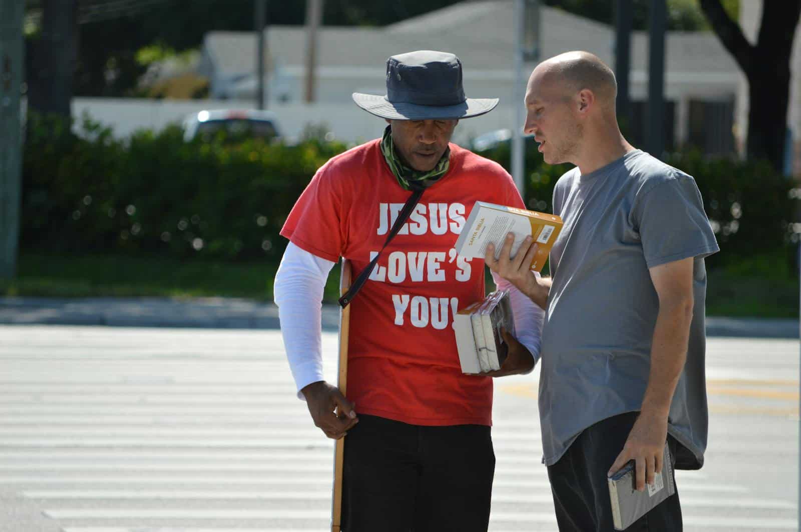 Two men engage in a religious conversation on a city street, holding books.