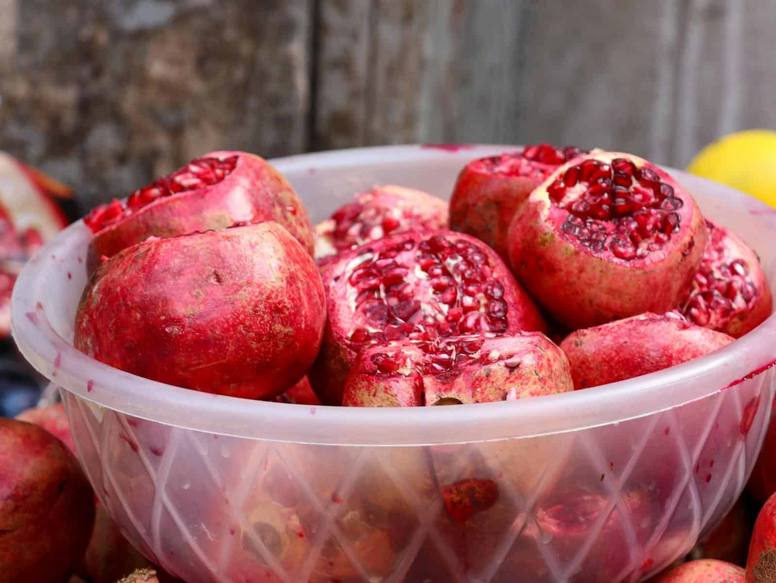 A close-up of fresh, cut pomegranates in a plastic bowl, showcasing vibrant red seeds.