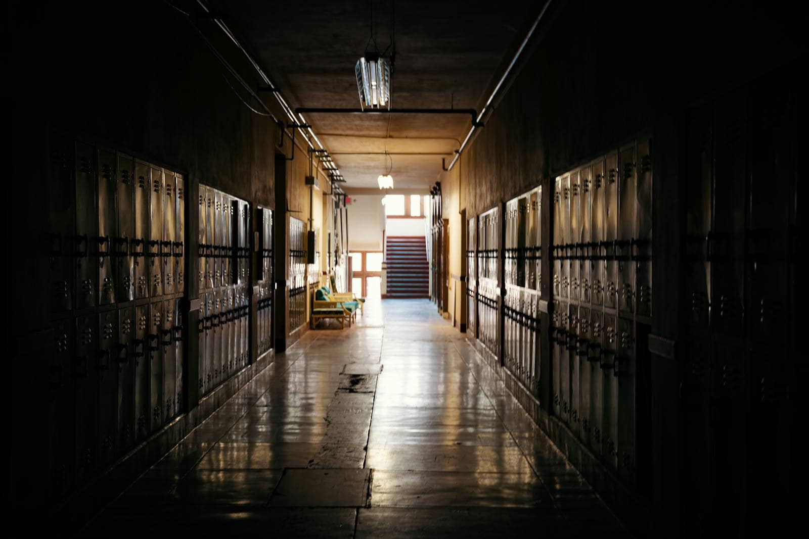 A dark and moody school hallway with lockers and a distant light source.