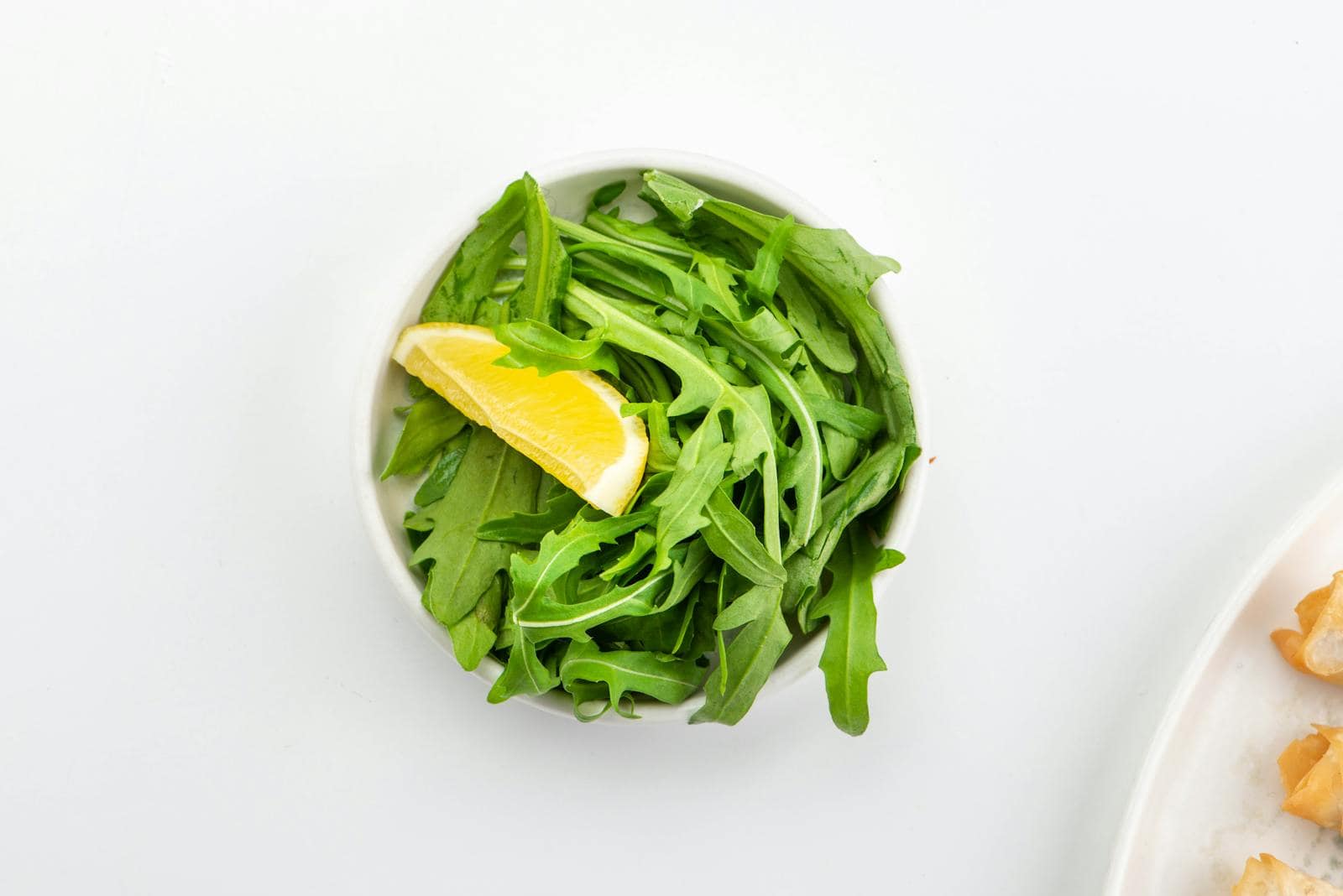 A fresh bowl of arugula topped with a lemon slice, perfect for a healthy meal.
