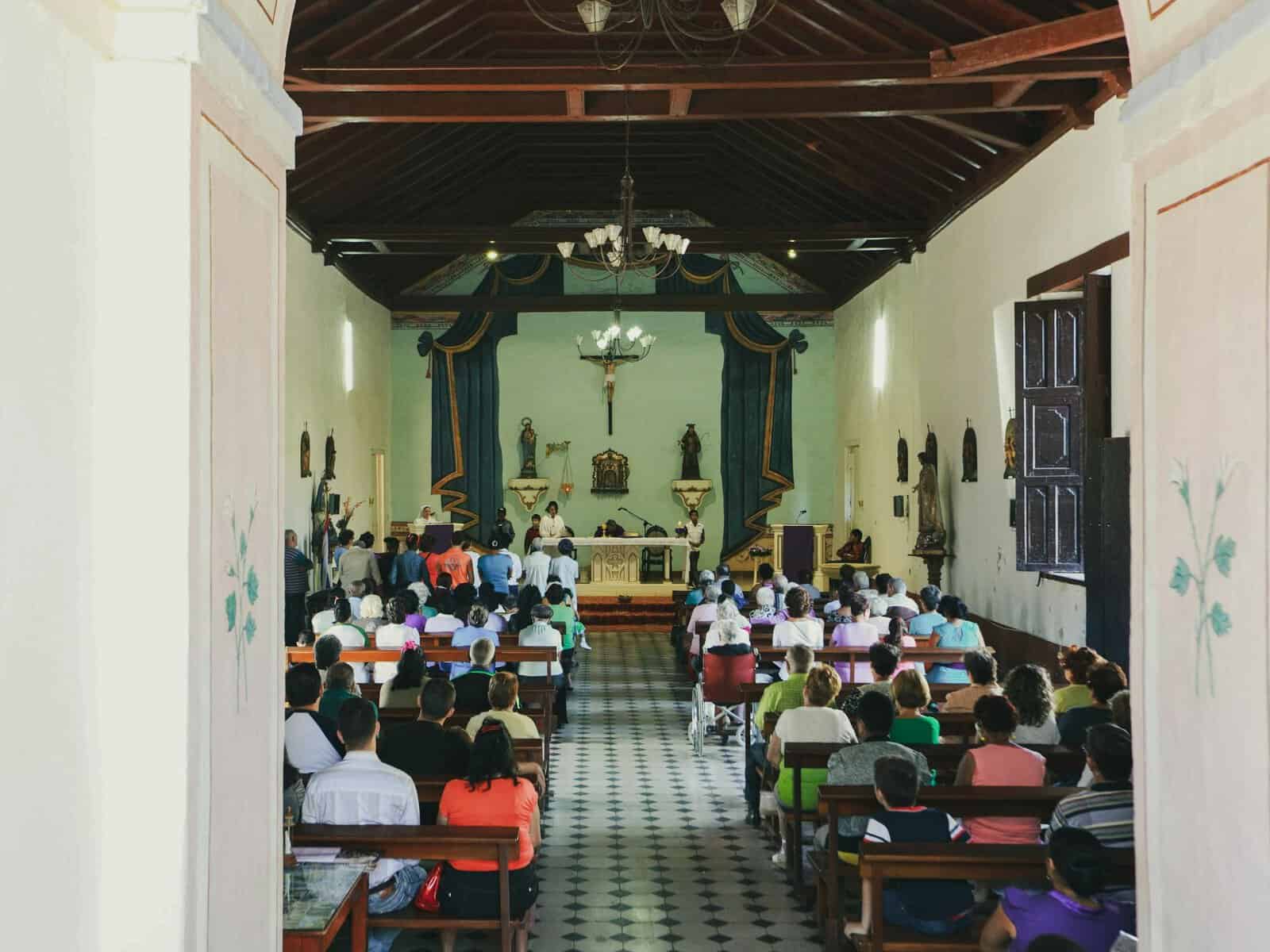 A full congregation participates in a Catholic mass at a traditional church.