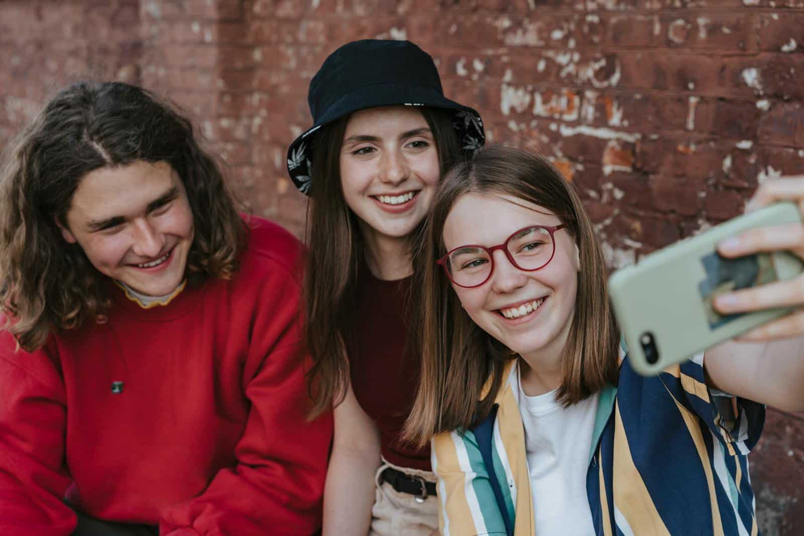 A group of happy teenagers taking a selfie outdoors against a brick wall.
