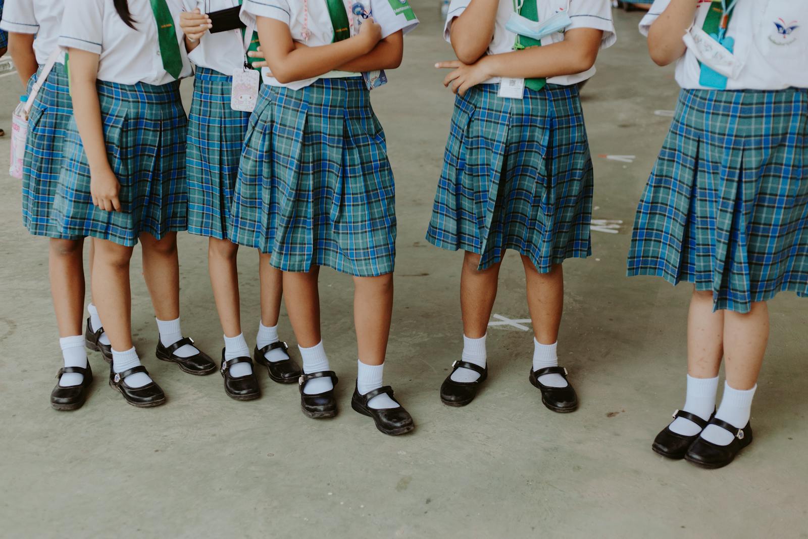 A group of schoolgirls standing in a corridor wearing plaid skirts and white shirts.