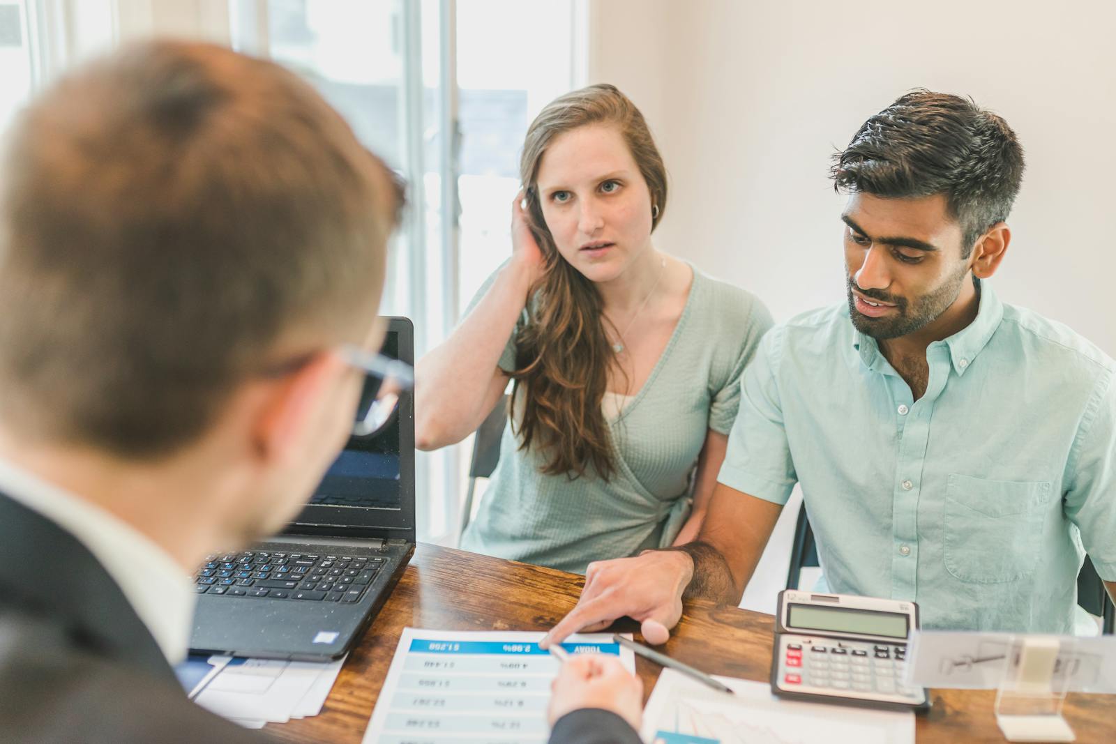A young couple consults with a realtor about buying a home, indoors in a modern office setting. Financial Advice